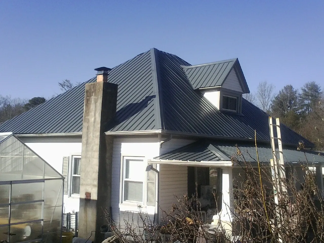 Dark blue standing seam metal roof on a white farmhouse with dormer — Slate & Tile Roof Repair by Roofing Brothers in Glen Oaks