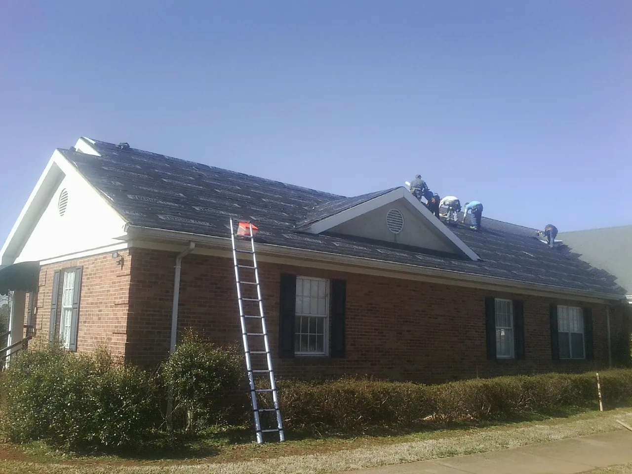 Crew tearing shingles off a brick ranch roof with a ladder set — Metal Roof Repair work by our crew in Glen Oaks