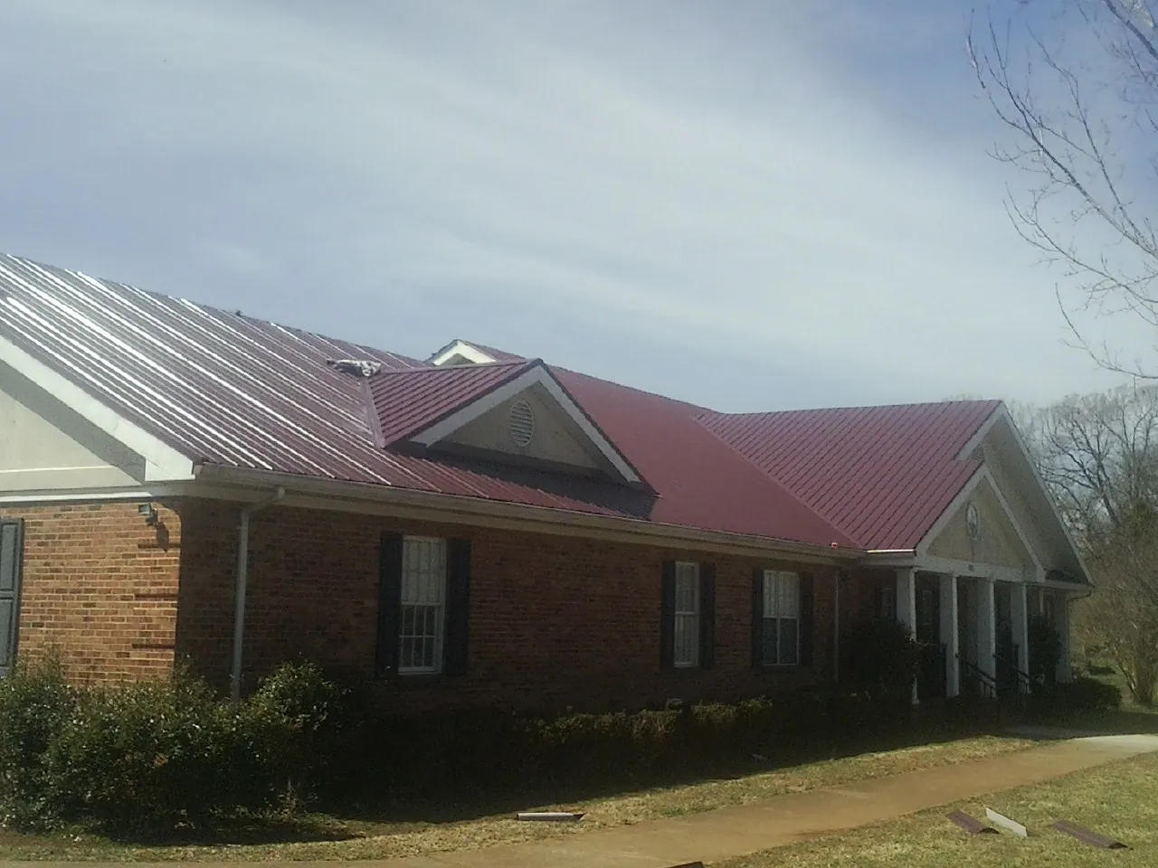 Red metal roof with gabled entries on a long brick building, from a Hail Damage Roof Repair job in Glen Oaks