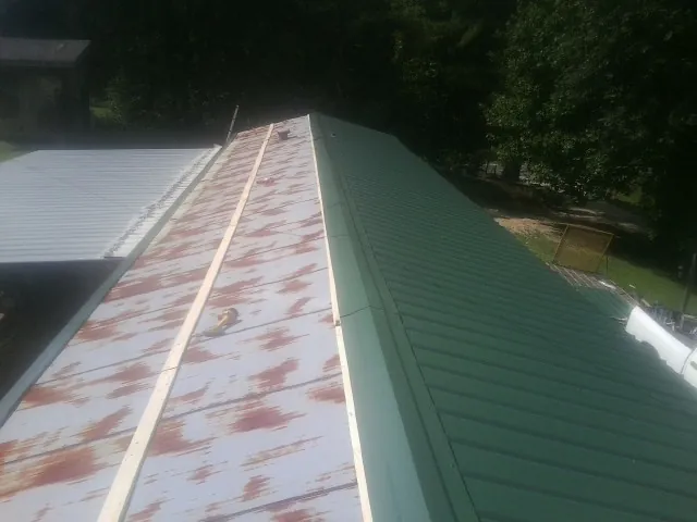Old rusted panels beside newly installed green metal roofing — Wind Damage Roof Repair by Roofing Brothers in Glen Oaks