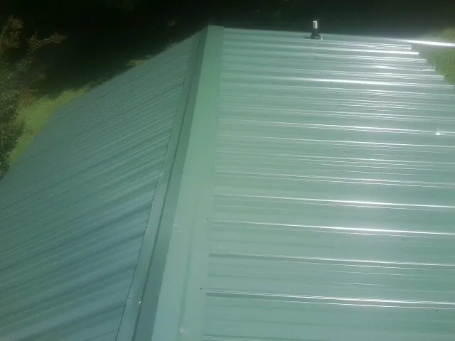 New green metal panels meeting at the ridge of a roof — Flat Roof Repair work by our crew in Glen Oaks