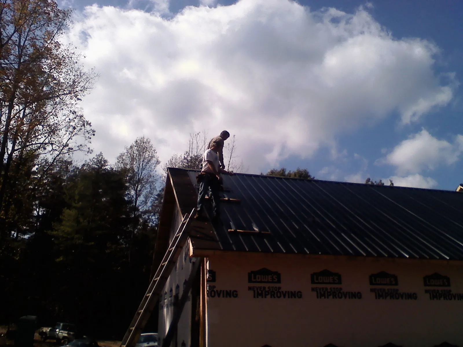 Roofer fastening dark metal panels high against a cloudy sky, from a Roof Inspection job in Glen Oaks
