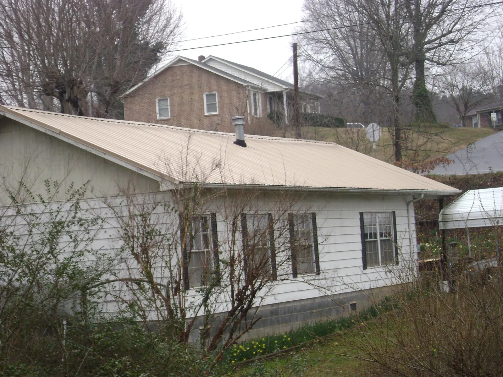 Tan metal roof on a white sided house set into a hillside — Commercial Roofing by Roofing Brothers in Glen Oaks