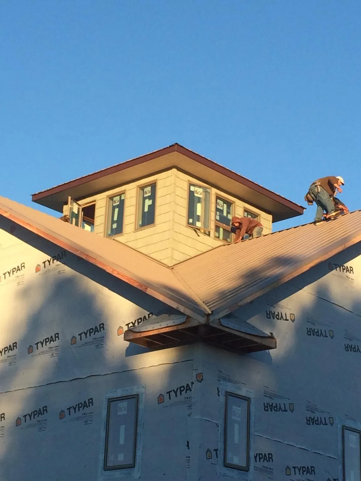 Roofers working around a rooftop cupola on a new metal roof at sunset — Roof Waterproofing in Glen Oaks by Roofing Brothers